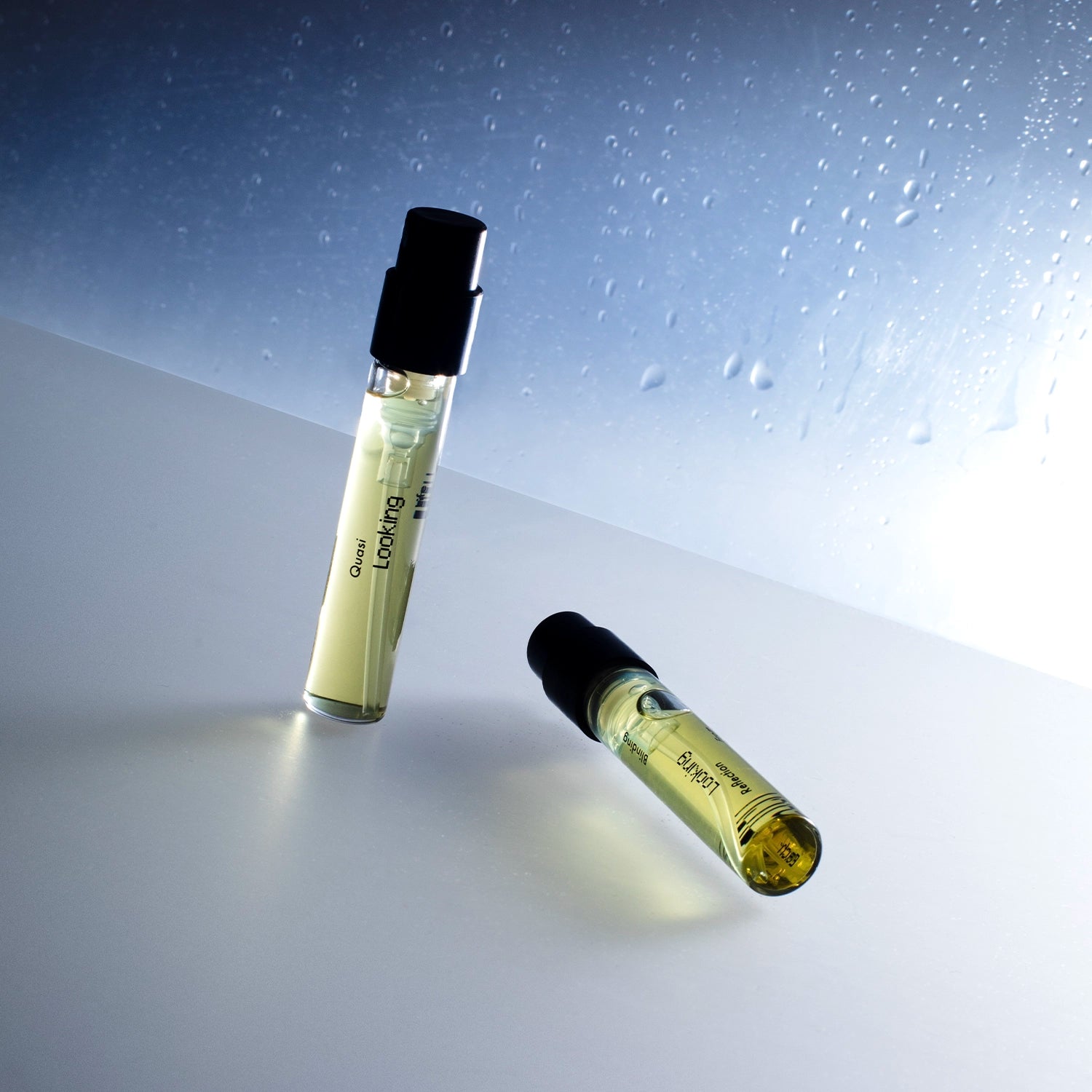 Discovery Duo fragrance vials from Looking for Each Other—Quasi Life in the Quasi World and Blinding Reflection from Tower Window—displayed against a misted glass backdrop, with soft lighting casting ethereal reflections on a smooth white surface.