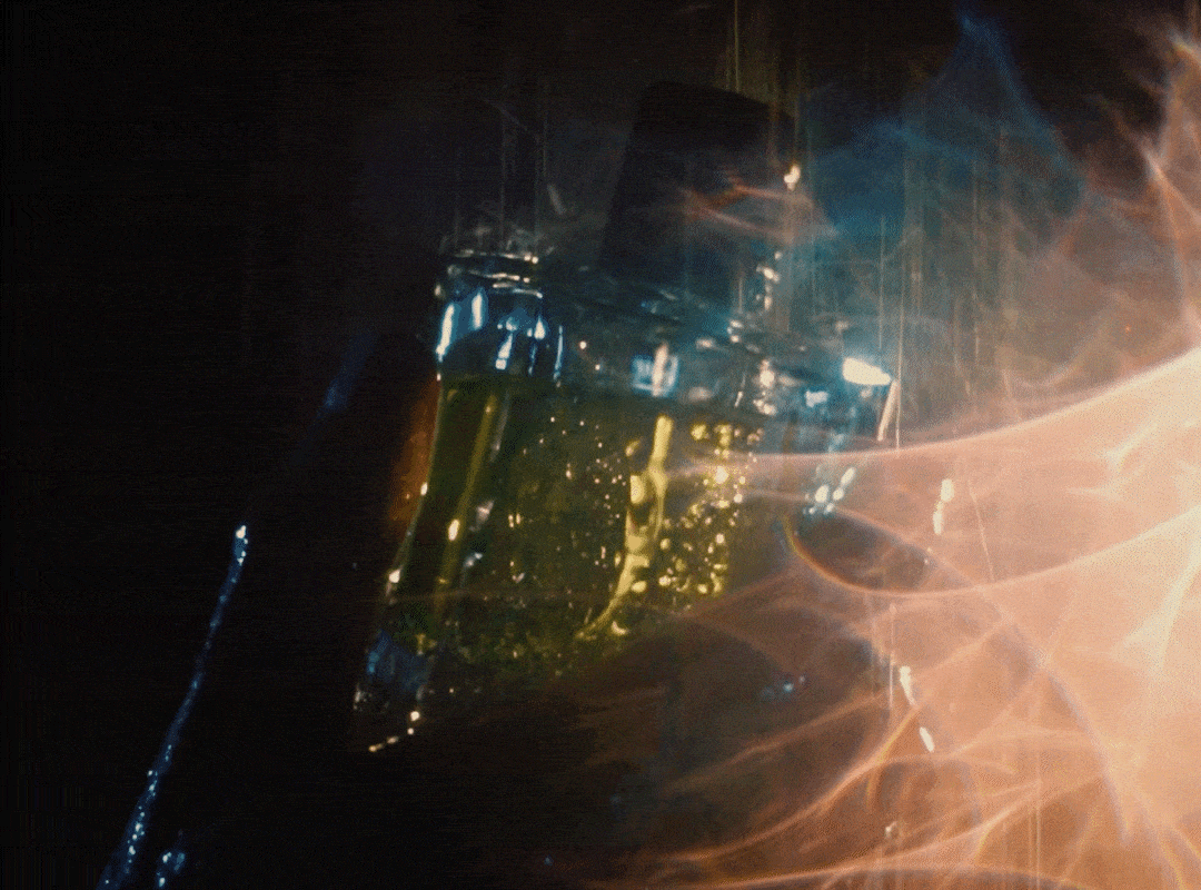 A hand holds a 50ml bottle of Looking for Each Other’s 100% botanical fragrance in the rain, glistening with blue reflections and touched by a red lens flare streaking in from the right—capturing the elemental beauty of scent in motion.