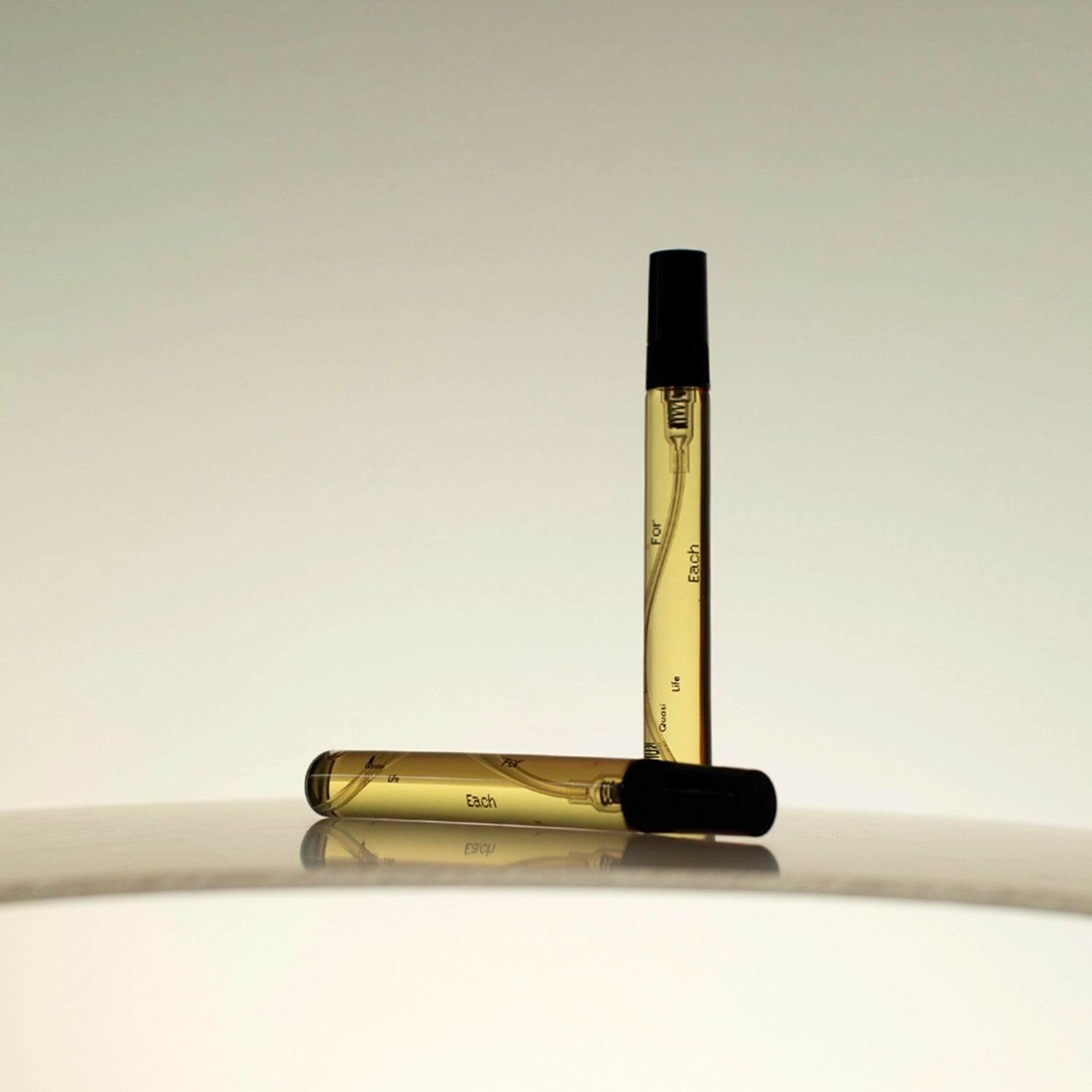 Two 10ml vials of Looking for Each Other – Quasi Life in the Quasi World perfume, standing and resting on a mirrored surface with warm light; minimalist glass packaging showcasing the brand’s genderless, botanical scent in travel-ready form.