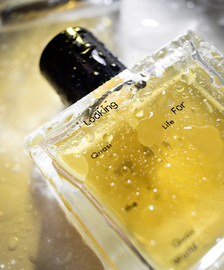 Close-up of a 50ml bottle of Quasi Life in the Quasi World by Looking for Each Other, covered in dewy water droplets. The yellow botanical liquid shines under soft light, reflecting the sacred and meditative tone of this 100% natural fragrance.